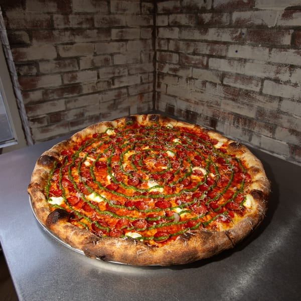 A Jonny's Pizza pepperoni pizza with pesto swirl and fresh mozzarella on a metal counter.