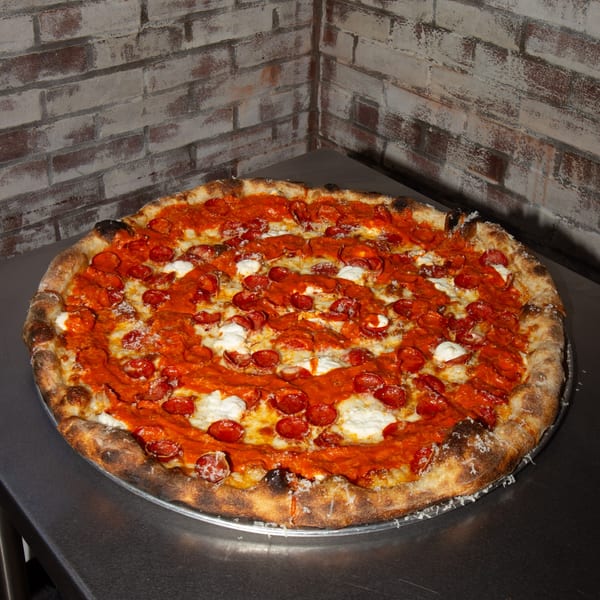A Jonny's Pizza pepperoni pizza with ricotta cheese on a metal tray against a brick wall.
