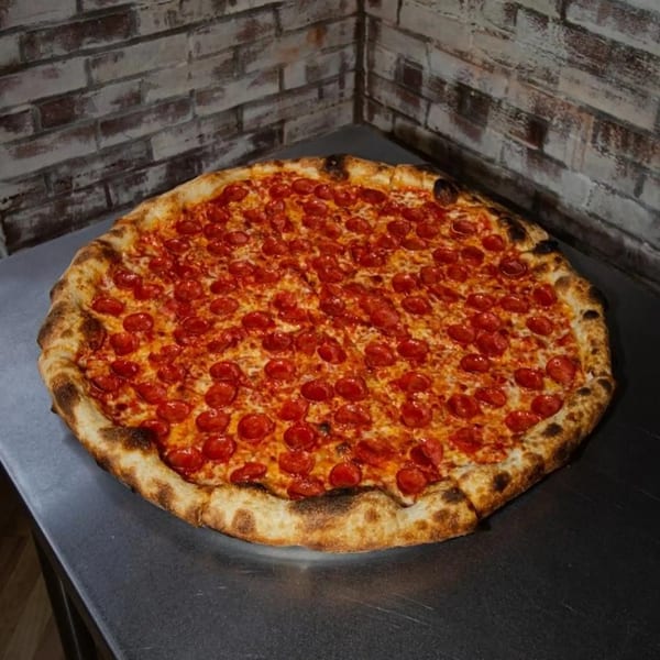 A large, round pepperoni pizza from Jonny's Pizza with a golden-brown crust on a metal surface.