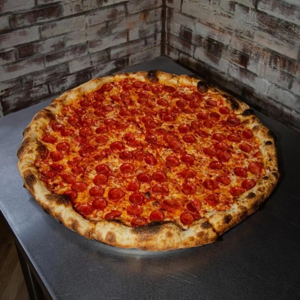 A large, round pepperoni pizza from Jonny's Pizza with a golden-brown crust on a metal surface.